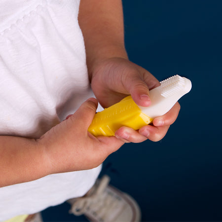 A cute toddler holding Baby Banana Toddler Toothbrush